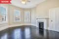 Before: Large room with three windows, black floors, beige walls, and old fireplace