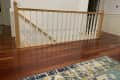 Wooden staircase railing with white spindles on polished hardwood floor, colorful rug in foreground.