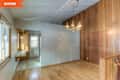 Empty dining room with wood panel walls, hardwood floor, and vintage chandelier. Adjacent area with a small counter and window.