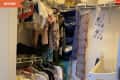 Closet with baby clothes on hangers, storage bins, and a crib.