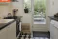 Narrow kitchen with black and white checkered floor, gas stove, and glass door leading to garden patio.