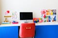 Colorful home office setup featuring a computer, pink chair, gold lamp, and vibrant decor elements.