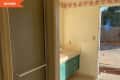 Before: Dated bathroom with standing shower, tan wallpaper and floors, and teal vanity