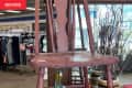 Wooden chair with a cracked seat in a thrift store, surrounded by clothing racks and decorative branches.