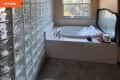 Before: Bathroom with tan walls, beige tile floor, a corner bathtub, and a walk-in shower surrounded by glass blocks