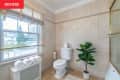 Bathroom with beige tiles, a white toilet, potted plant, rolled towels on a radiator, and a window with blinds.