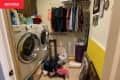 Wood cabinets with washer and dryer below, messy top with detergent and cleaning supplies everywhere, hanging clothes on rack, pile of clothes on floor