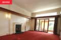 Empty living room with wood trim on walls, glass doors, and windows, dark marble fireplace, and red carpeting.