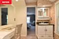 Bright bathroom with floral wallpaper, white vanity, green countertop, and a view into a cozy bedroom.
