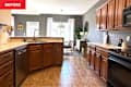 Kitchen with wooden cabinets, stainless steel dishwasher, and a dining area featuring a round table and plants.