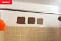 Three brown paint swatches on a white wall above beige tiled shower, with an orange loofah hanging nearby.