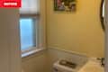 Small bathroom with yellow walls, a window with blinds, a round mirror, and a toilet with a tray of soaps.