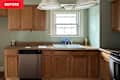 Kitchen with wooden cabinets, stainless steel dishwasher, sink with blue tape, and light fixtures above.