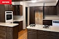 Kitchen with dark wood cabinets, white countertops, a built-in oven, and a gas cooktop on an island.