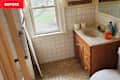 Small bathroom with a sink, wooden cabinet, toilet, and window, featuring white tiles and cleaning supplies.