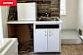 A small kitchen area with a white mini fridge, sink, and open cabinet space, featuring exposed wooden walls and unfinished flooring.