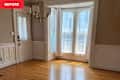 A bright room with hardwood floors, large windows with sheer curtains, and a modern chandelier.