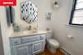 Bathroom with light blue vanity, hexagonal mirror, white toilet, and decorative wall art.