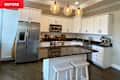 Modern kitchen with white cabinets, stainless steel appliances, black countertops, and three pendant lights above an island with stools.