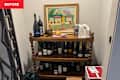 Wooden shelf displaying various wine bottles, a decorative painting, and a metal bucket, with a green bag nearby.