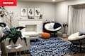 Cozy living room with a white sofa, blue patterned rug, two round chairs, and a fireplace adorned with plants and decor.