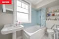 Bathroom featuring a white pedestal sink, blue tiled shower area, and a bathtub, with shelves of toiletries.