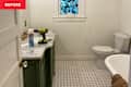 Bathroom with green vanity, marble countertop, drill, cleaning spray, and stained glass window. White toilet and hexagonal tile floor.