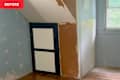 A corner of a room with unfinished walls, a dark blue cabinet door, and a window letting in natural light.