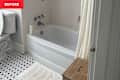 Bathroom with a white bathtub, shower curtain, wooden stool, and black and white tiled floor.