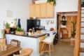 Cozy kitchen with black fridge, wooden cabinets, plants, and a small dining area with wooden table and chairs.