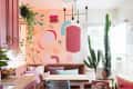Colorful dining nook with abstract wall art, pink cabinets, wooden table, large cactus, and hanging plants.