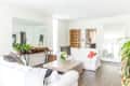 Bright living room with white sofas, wooden coffee table, large mirrors, and green plants on a console table.