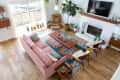 Living room with pink sofa, colorful rug, wooden coffee table, plants, and a white fireplace under a mounted TV.