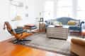 Living room with blue velvet sofa, patterned cushions, Eames lounge chair, metal coffee table, and abstract wall art.