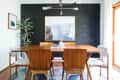 Dining room with wooden table, six chairs, black accent wall, large framed artwork, and a potted plant.