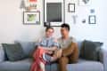Couple sitting on a gray sofa, surrounded by framed art and decor on the wall.