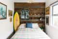 Bedroom with wood accent wall, vintage tennis rackets, Taxi Driver poster, surfboard, and plaid bedspread.
