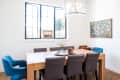 Dining room with wooden table, gray chairs, blue armchairs, chandelier, and colorful wall art.