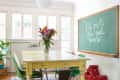 Dining room with a yellow table, green chairs, colorful flowers, and a chalkboard with handwritten text.