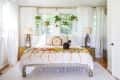 Bohemian bedroom with a cat on a colorful bedspread, hanging plants, and decorative lamps on side tables.