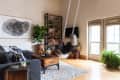 Living room with a gray sofa, wooden coffee table, bookshelf, large plant, and a person swinging near French doors.