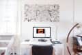 Home office with a white desk, computer displaying a video, abstract wall art, and a curved floor lamp.