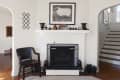 White brick fireplace with black screen, framed sheep art, decorative vases, and a wooden chair in a living room.
