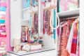 Pink closet with white dresser, colorful jewelry, and vibrant clothing, including a yellow dress and patterned shirts.