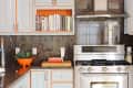Modern kitchen with stainless steel stove, gray cabinets with orange trim, books, and an orange bowl with greens.