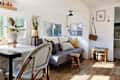 Cozy RV interior with a gray sofa, wooden stools, potted plants, and a dining table with wicker chairs.
