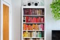 Bookshelf with color-coordinated books, a stereo, and a fan on top, next to a green plant and a wooden door.