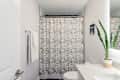 Bathroom with geometric shower curtain, snake plant on counter, and towel on rack.