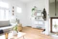 Bright living room with a gray sofa, gold trunk, white shelves, and plants on hardwood floor.