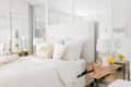 White bedroom with mirrored walls, plush pillows, gold-accented side tables, and yellow flowers in vases.